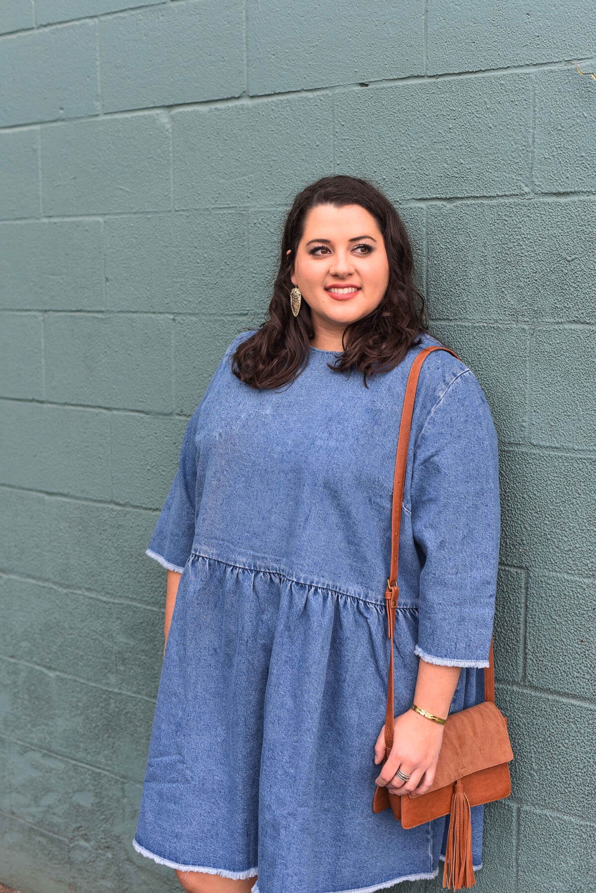 Spring style in a denim dress. Emily Bastedo, curvy style blogger from Something Gold, Something Blue features this comfortable and versatile dress perfect for running errands or a night on the town. She's currently ready to go to brunch with a statement heel, small clutch and bold earrings. Brunch style, spring style, plus size style, plus size fashion, floral